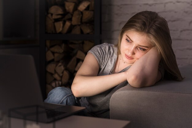 Blonde Frau, die auf einer Couch mit Laptop sitzt