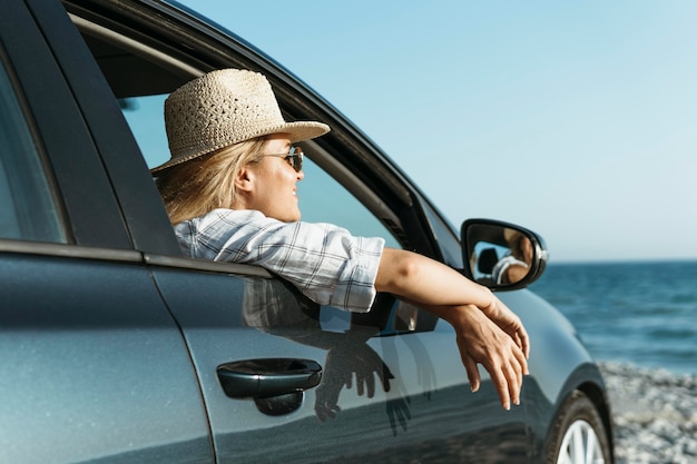 Blonde Frau, die aus Autofenster schaut, das Meer betrachtet