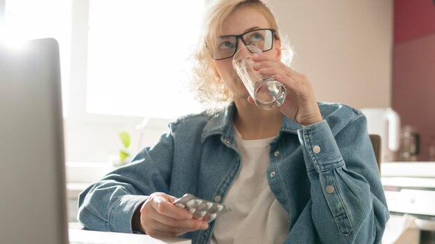 Blonde Frau, die eine Pille nahe Laptop nimmt