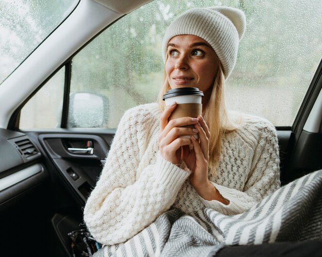 Blonde Frau, die eine Tasse Kaffee in einem Auto hält