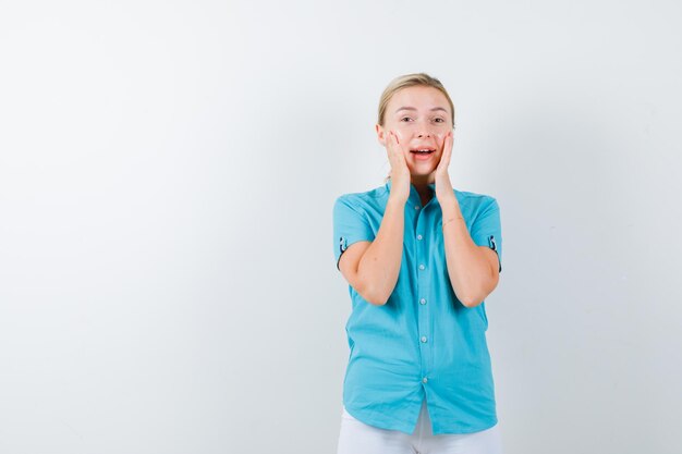 Blonde Frau, die Hände auf Wangen in blauer Bluse hält und glücklich isoliert aussieht looking