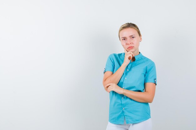 Blonde Frau, die Hand am Kinn in blauer Bluse hält und nachdenklich isoliert aussieht