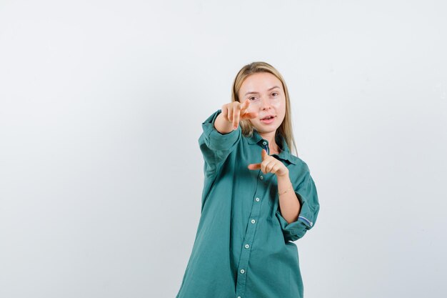 Blonde Frau, die im grünen Hemd auf die Kamera zeigt und selbstbewusst aussieht looking