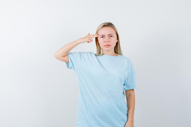 Blonde Frau, die in blauem T-Shirt eine Waffengeste in der Nähe des Kopfes zeigt und ernst aussieht