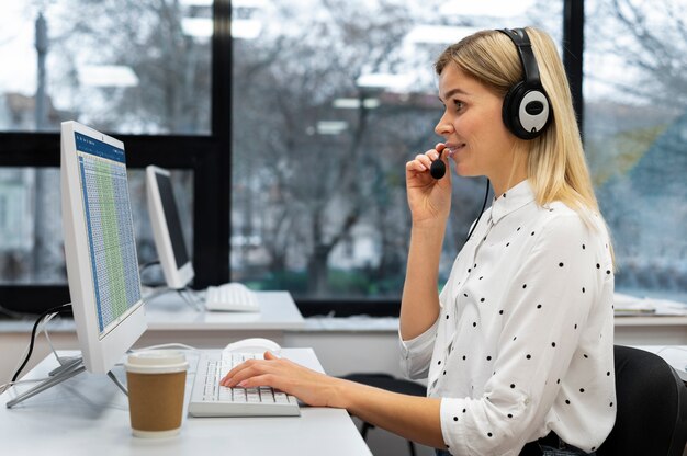 Blonde Frau, die in einem Callcenter mit Kopfhörern und Computer arbeitet