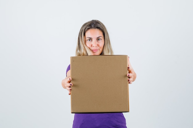 blonde Frau, die Pappkarton in der Vorderansicht des violetten T-Shirts zeigt.