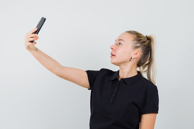 Blonde Frau, die selfie im schwarzen T-Shirt nimmt