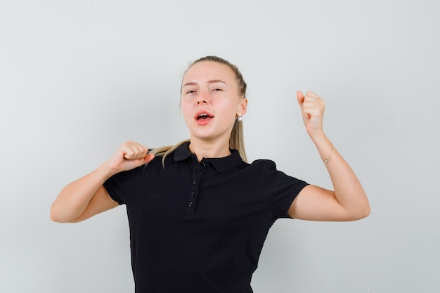 Blonde Frau, die sich im schwarzen T-Shirt streckt und gähnt und schläfrig aussieht