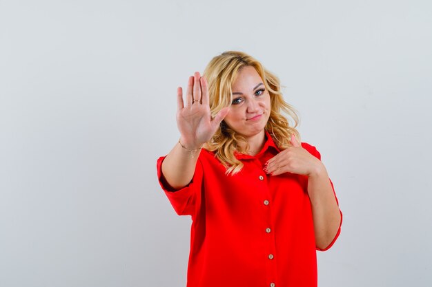 Blonde Frau, die Stoppschild in der roten Bluse zeigt und glücklich schaut.