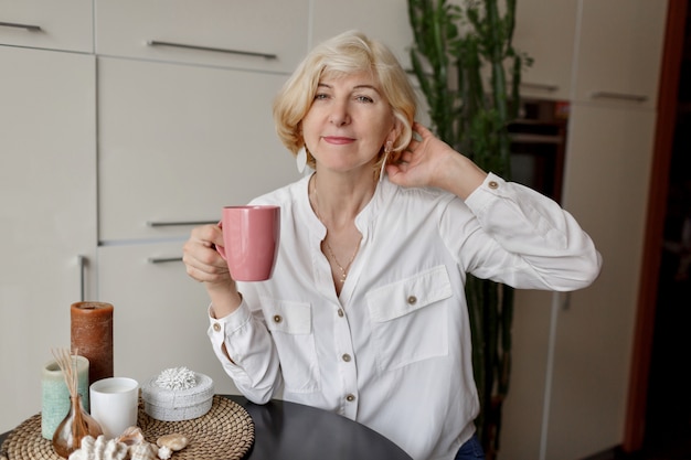 Blonde Frau, die Tasse Tee hält und an der modernen Küche sitzt