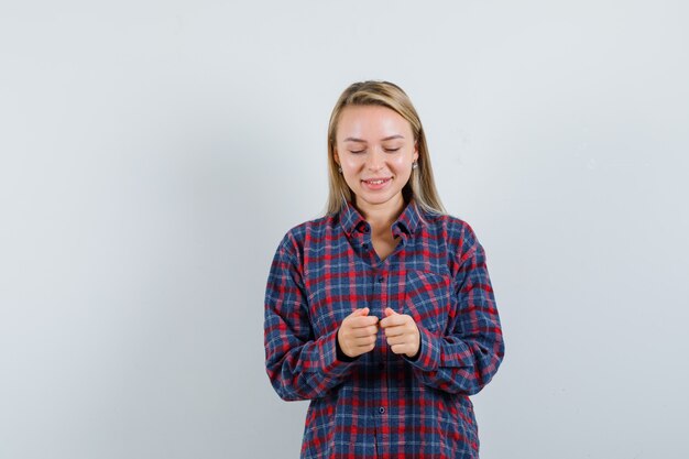 Blonde Frau, die vorgibt, mit Telefon im karierten Hemd zu spielen und optimistisch, Vorderansicht schauend.