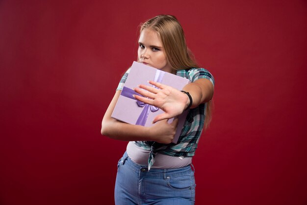 Blonde frau hält eine geschenkbox fest und wird eifersüchtig auf das teilen.