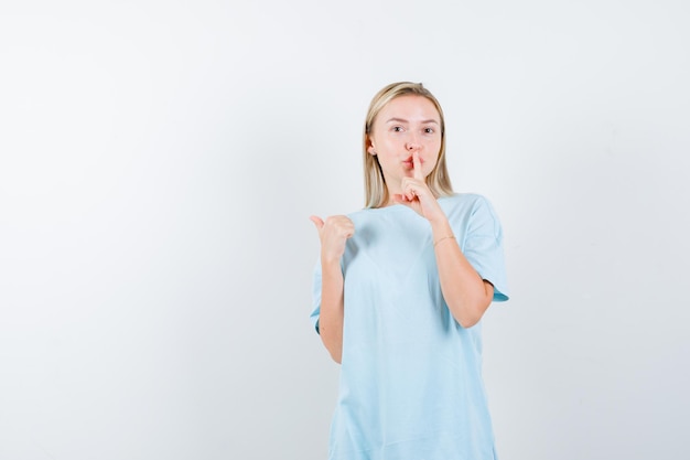 Blonde Frau im blauen T-Shirt, die Stillegeste zeigt und mit dem Daumen zur Seite zeigt