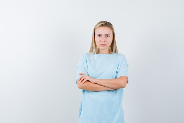 Blonde Frau im blauen T-Shirt mit verschränkten Armen und ernstem Blick