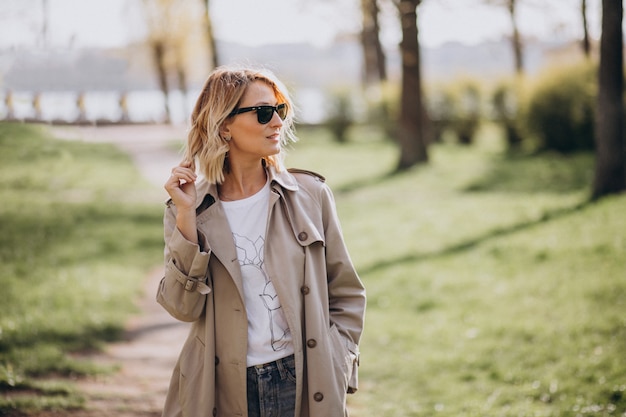 Blonde Frau im Mantel draußen im Park