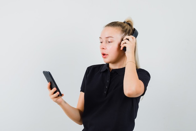 Blonde Frau im schwarzen T-Shirt, das Musik mit Kopfhörern hört