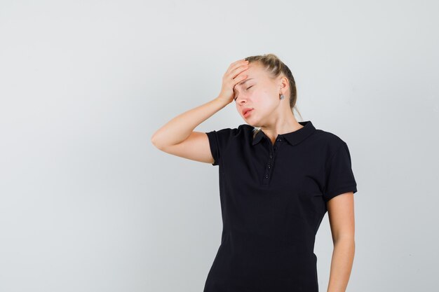 Blonde Frau im schwarzen T-Shirt, die ihre Hand auf ihren Kopf legt und genervt aussieht