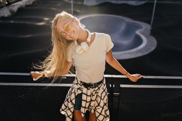 blonde Frau im T-Shirt, das mit glücklichem Lächeln im Skatepark aufwirft.