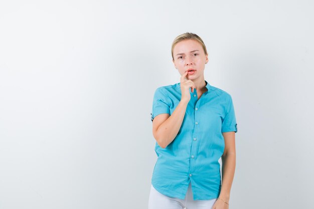 Blonde Frau in blauer Bluse, die das Kinn auf der Hand stützt und nachdenklich isoliert aussieht