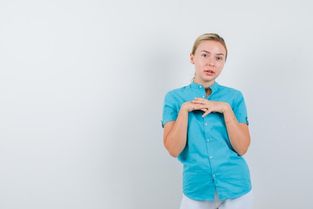 Blonde Frau in blauer Bluse, die die Hände über die Brust hält und zart isoliert aussieht