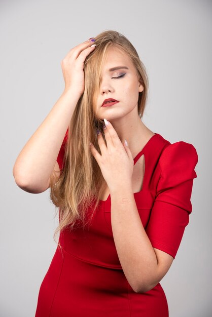 Blonde Frau in der roten Ausstattung, die ihr Haar hält.