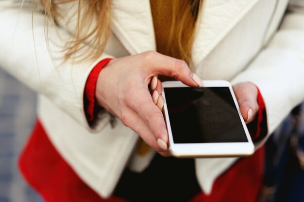 Blonde Frau in der weißen Jacke macht ein Foto an ihrem Telefon