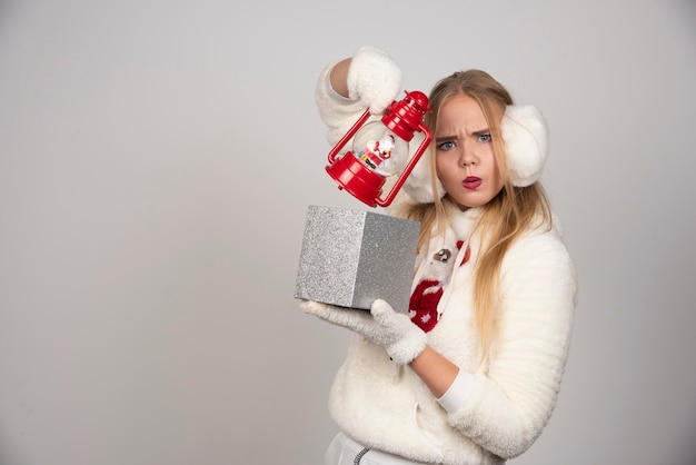 Blonde Frau in der weißen Strickjacke, die ihr Geschenk zeigt.