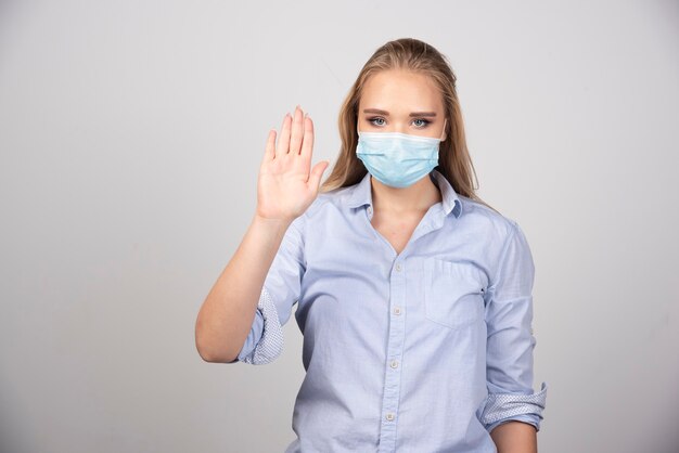 blonde Frau in medizinischer Maske, die Nummer fünf mit der Hand zeigt.