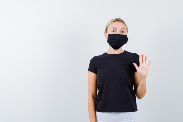 Blonde Frau in schwarzem T-Shirt, weißer Hose, schwarzer Maske mit Stoppschild