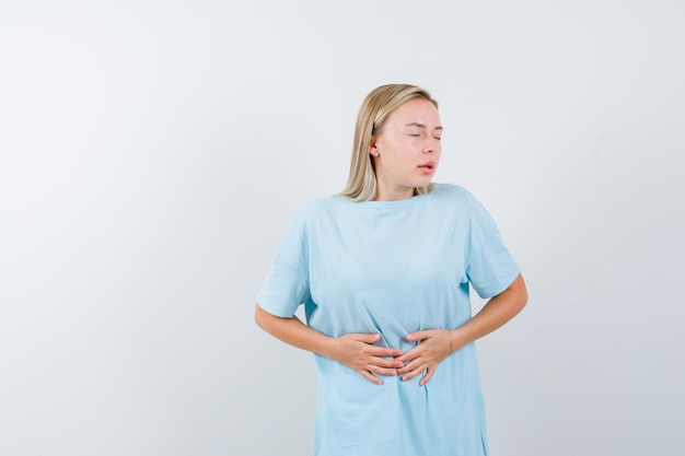 Kostenloses Foto blonde frau legt sich die hände auf den bauch und hat bauchschmerzen im blauen t-shirt