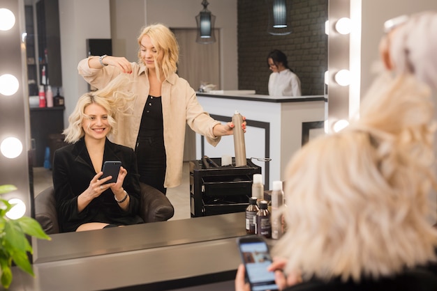 Kostenloses Foto blonde frau mit dem handy, der ihr haar erledigt erhält