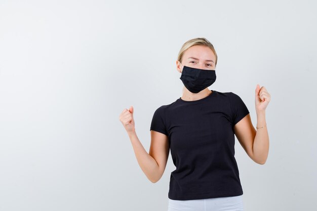 Blonde Frau mit Gewinnergeste in schwarzem T-Shirt, weißer Hose