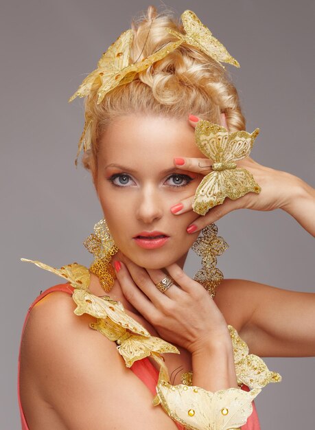 Blonde Frau mit goldenem Schmetterling. Isoliert auf grauem Hintergrund.