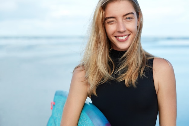 Blonde Frau mit Surfbrett am Strand