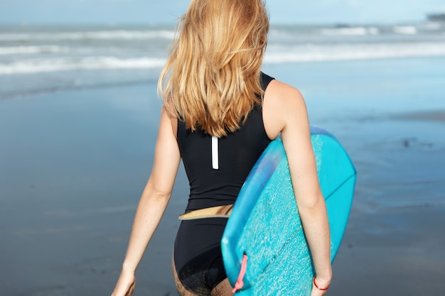 Blonde Frau mit Surfbrett am Strand