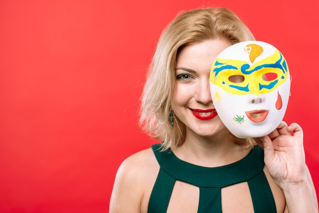 Blonde Frau mit weißer Karnevalsmaske in der Hand