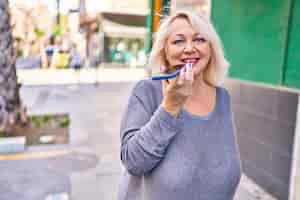 Kostenloses Foto blonde frau mittleren alters lächelt zuversichtlich und spricht auf der straße mit dem smartphone