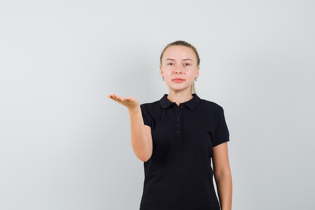 Blonde Frau tippt ihre Hand in schwarzem T-Shirt und sieht optimistisch aus