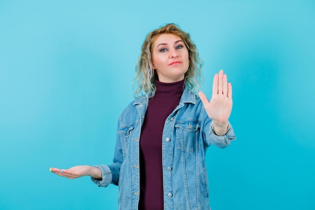 Blonde Frau zeigt Stop-Geste mit der Hand auf blauem Hintergrund