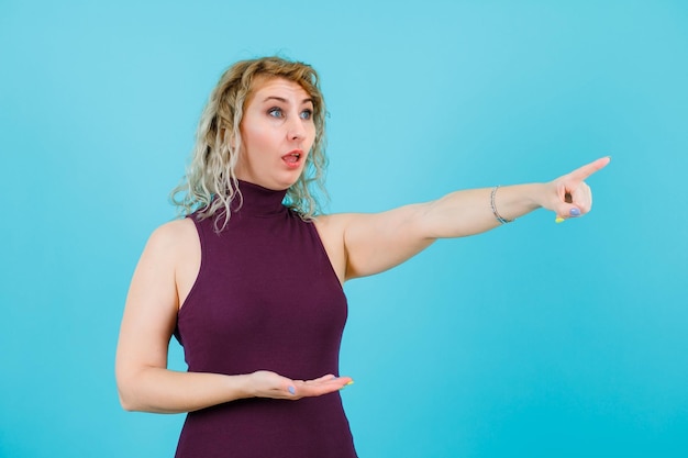 Blonde Frau zeigt weg, indem sie auf blauem Hintergrund wegschaut