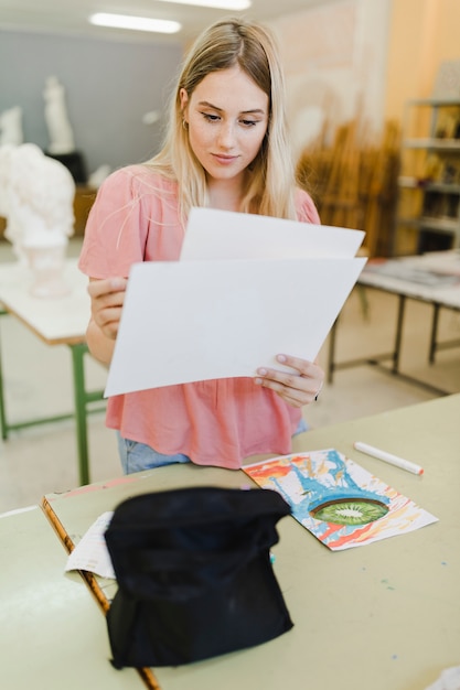 Blonde junge Frau, die das Segeltuchpapier steht hinter der Tabelle betrachtet