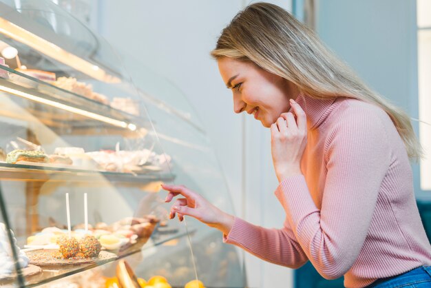 Blonde junge Frau, die durch Kuchenvitrine im Café schaut