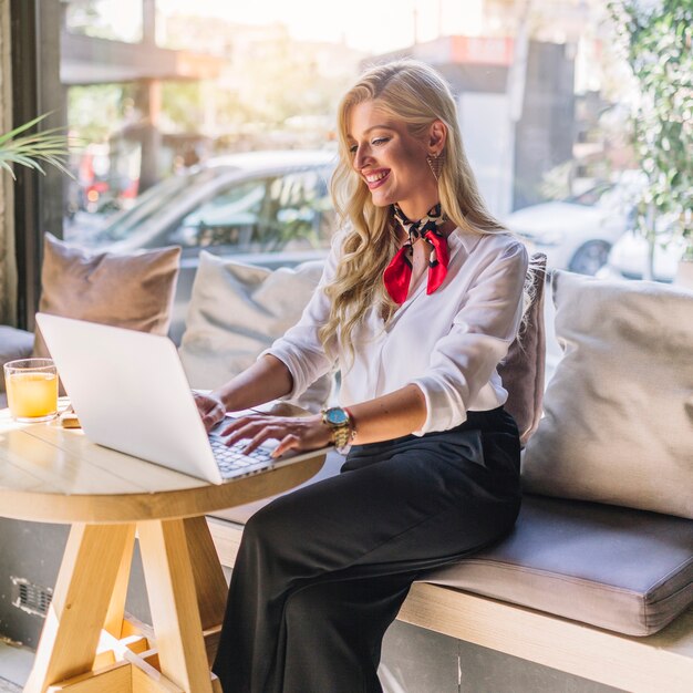 Blonde junge Frau, die im caf� unter Verwendung des Laptops sitzt