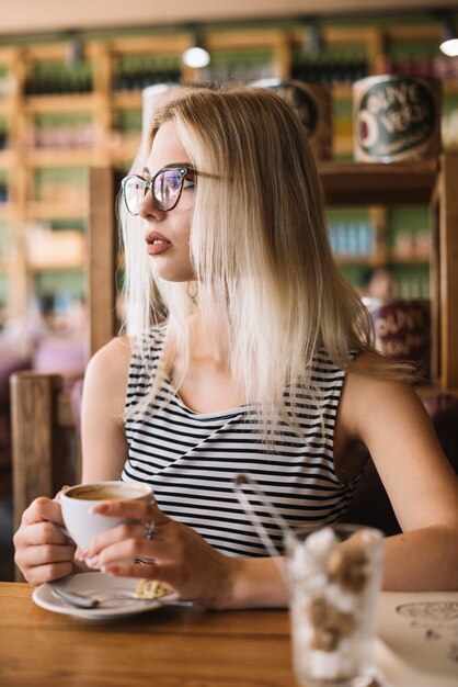 Blonde junge Frau, welche die Kaffeetasse weg schaut im cafÃ © hält