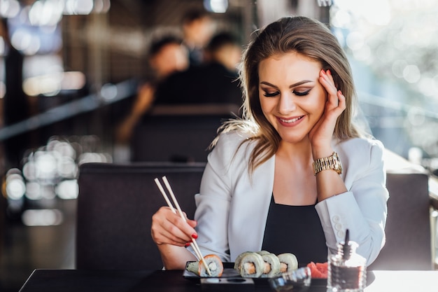 Blonde, junge schöne blonde Mädchengeschäftsfrau, die Sushi auf der Sommerterrasse in einem japanischen Restaurant isst.