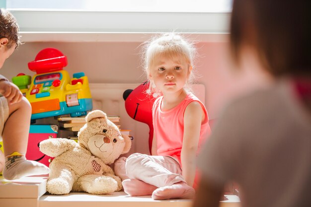 Blonde kleine Mädchen sitzen im Spielzimmer starrte