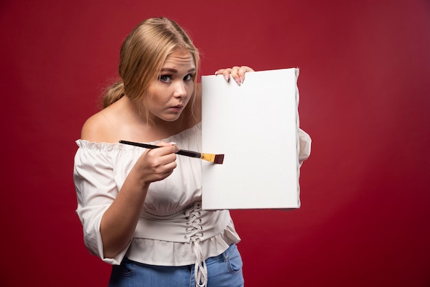 Kostenloses Foto blonde künstlerin, die zögernd ihre kunstwerke zeigt und nach rezensionen sucht.