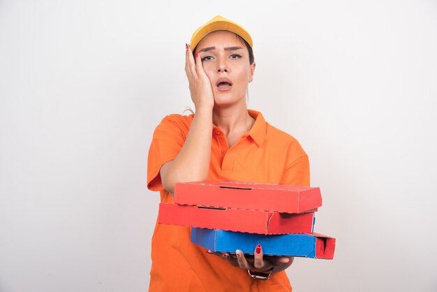 Blonde Lieferfrau, die ihr Gesicht und Pizzaschachteln auf weißem Hintergrund hält.