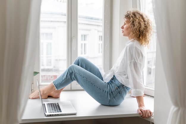 Blonde lockige Frau, die zu Hause in der Nähe des Fensters entspannt