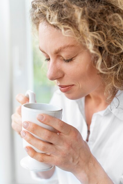 Blonde lockige Frau, die zu Hause in der Nähe des Fensters entspannt